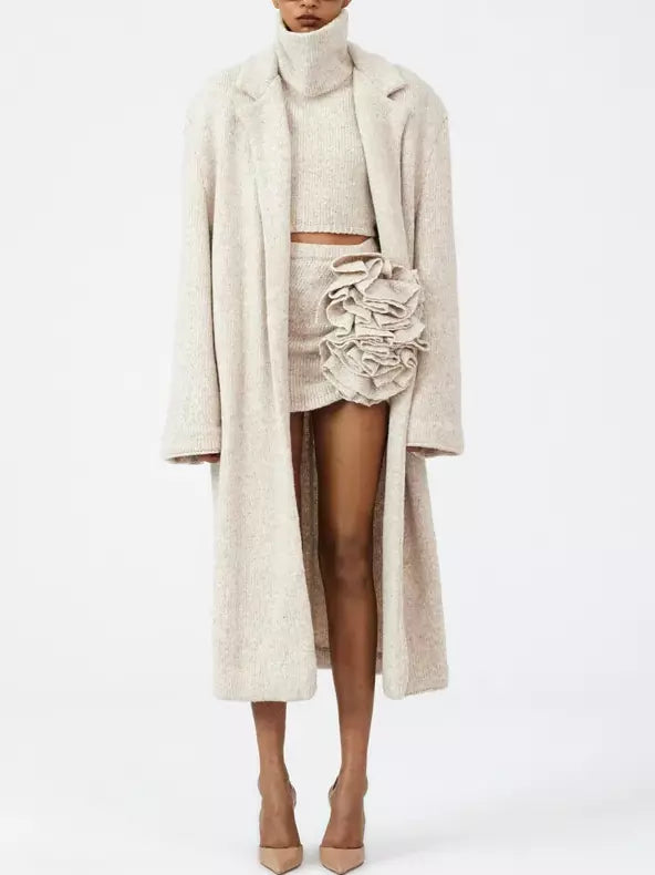 Woman’s cream outfit featuring a sleeveless turtleneck and flower applique skirt with overcoat