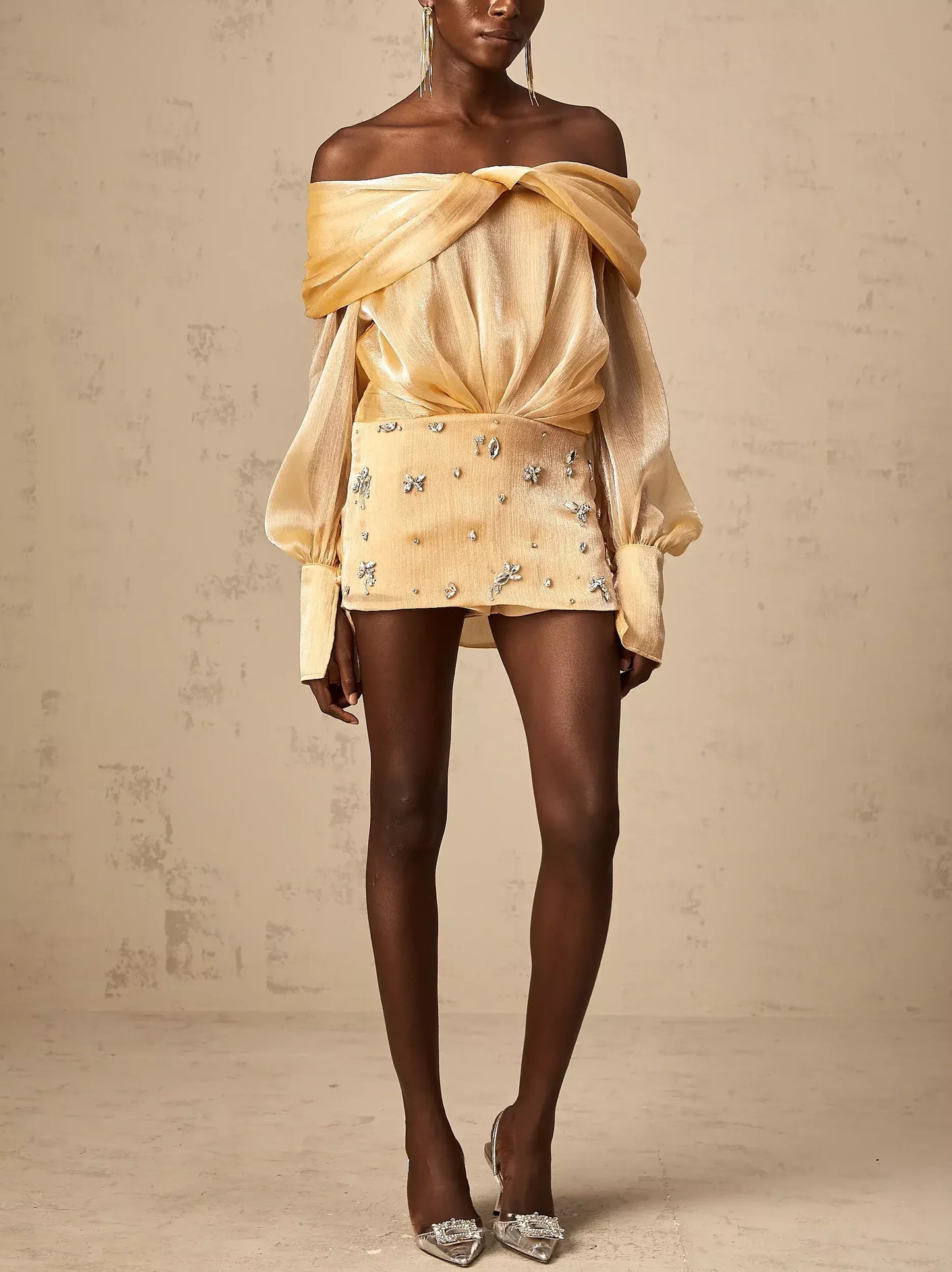 Woman in luxurious satin gold off-shoulder mini dress adorned with rhinestones