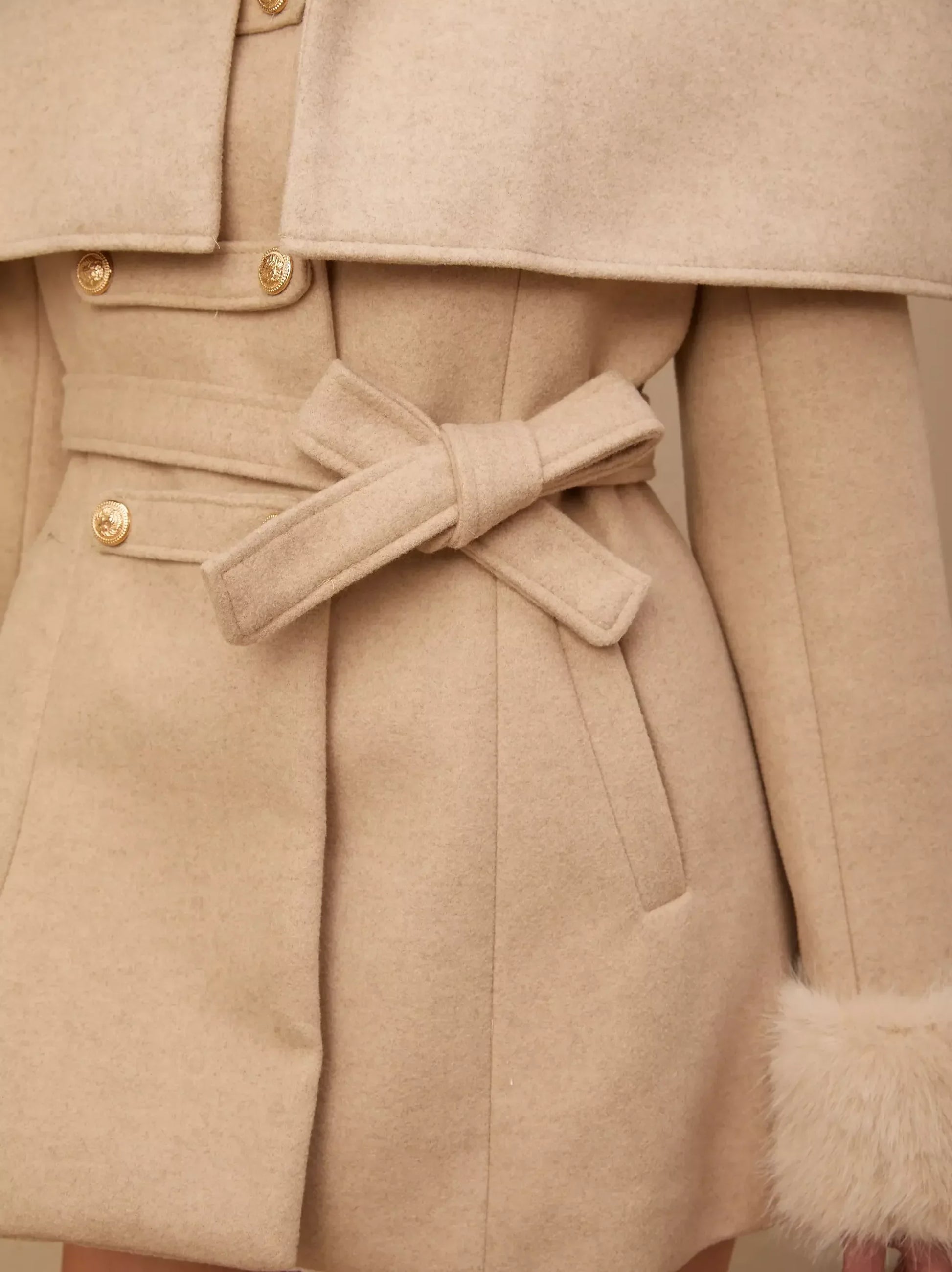 Cream-colored belted coat showcasing a detachable faux-fur cape for versatile style