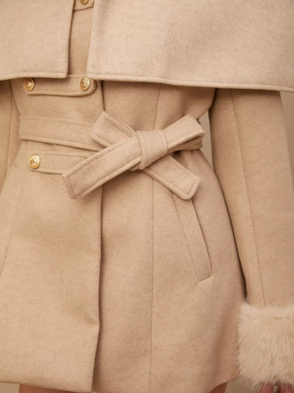 Cream-colored belted coat showcasing a detachable faux-fur cape for versatile style