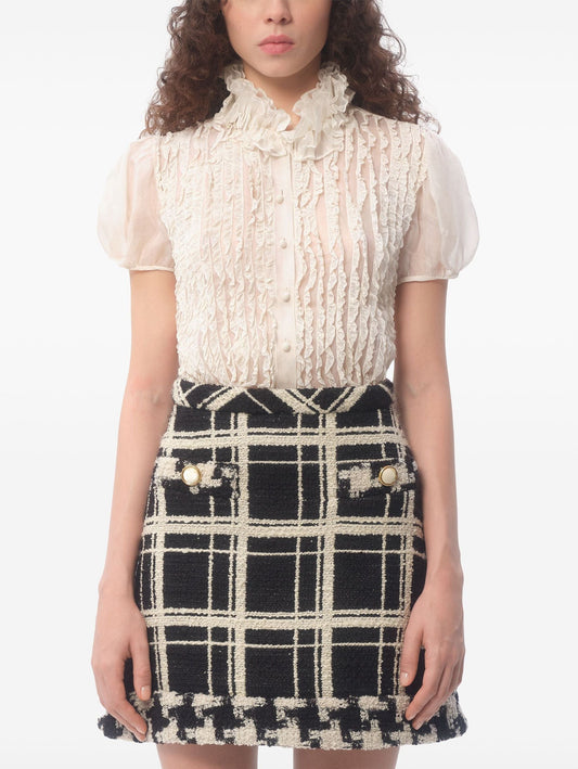 Woman in a ruffle silk organza short sleeve blouse styled with a plaid skirt